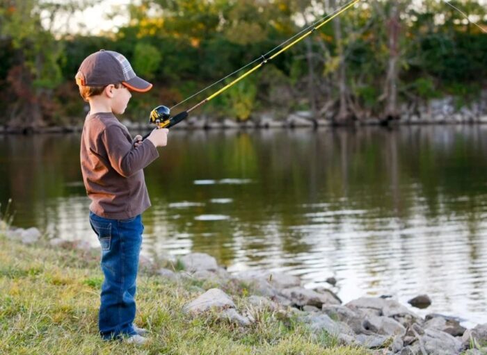 Beginner child practicing fishing with adult supervision on a dock.
