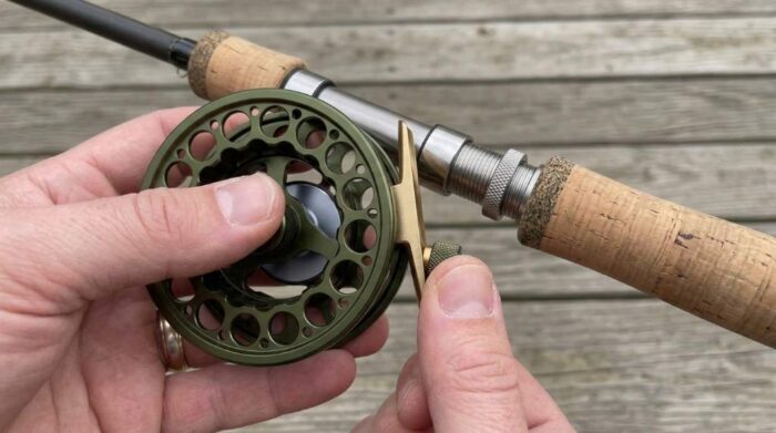 Fly fisher adjusting rear cork drag dial while wading pristine trout stream.